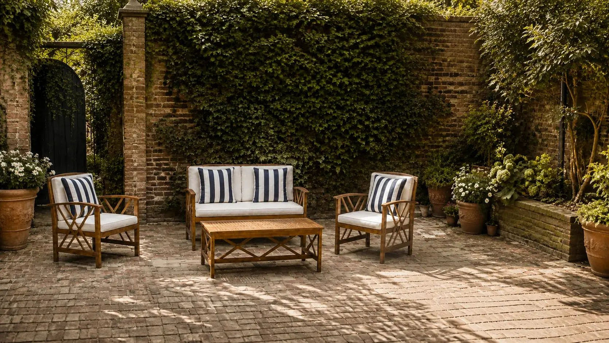 Four-piece acacia patio set with a compact loveseat, two fan-lattice armchairs, four striped navy pillows and a slatted table in a sunlit brick garden.