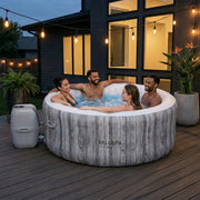 Patio | Four adults relaxing in the bubbling spa on a lit patio at dusk