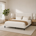 Bedroom scene | Upholstered bed in a bright corner with a window, plant, and light wood furniture