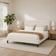 Bedroom scene | Upholstered bed in a bright corner with a window, plant, and light wood furniture