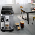 Lifestyle | Magnifica Evo espresso machine with LatteCrema carafe on a dining table pouring a latte macchiato with iced coffee and espresso nearby