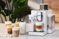 Lifestyle | white Rivelia on a countertop pouring an iced latte, with iced coffee drinks lined up beside it