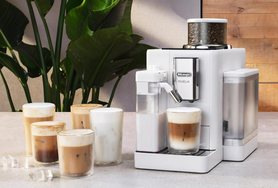 Lifestyle | white Rivelia on a countertop pouring an iced latte, with iced coffee drinks lined up beside it