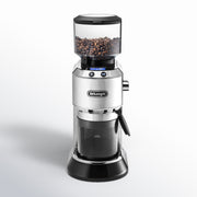Front | silver Dedica conical burr grinder with beans in the hopper and the grounds container fitted below the chute
