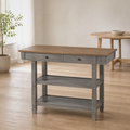 In a room | antique-gray kitchen island with an oak-wood top, two drawers and two open shelves, freestanding beside a warm oak dining room's round table, window at left