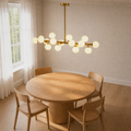 Angle | second angle of the Marnau Glazenn 16-light sputnik chandelier over the round wood dining table, showing the fixture's staggered globes from the side