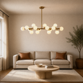 In a room | marnau Glazenn 16-light sputnik chandelier hung in a living room above a beige sofa with leather pillows and a round travertine coffee table