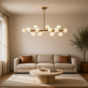 In a room | marnau Glazenn 16-light sputnik chandelier hung in a living room above a beige sofa with leather pillows and a round travertine coffee table
