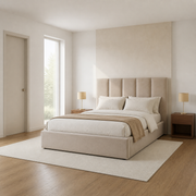In scale | Beige upholstered bed in a pale bedroom with a full-height doorway and window visible for scale