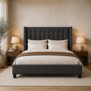 Warm bedroom | Charcoal button-tufted wingback bed with silver nailhead trim, walnut nightstands, and a plain ivory rug
