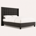 Studio angle | Charcoal button-tufted wingback bed from the front left with a low upholstered footboard and short dark feet