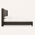 Studio side | Charcoal wingback bed in full left-side profile with white bedding, a low side rail, and short dark feet