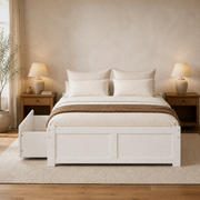 In a room | White storage platform bed styled with neutral bedding, wood nightstands, lamps, and a warm area rug