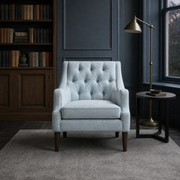 Blue-gray library | pale ice-blue tufted wingback chair with a dark wood bookcase and brass floor lamp
