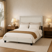 Angle | Three-quarter view of the cream upholstered bed with wood nightstands and window