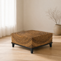 In a room | square brown wicker coffee table with black wood legs on a pale oak floor near a sofa