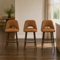 In a room | all three matching counter stools at a plaster dining room's kitchen island edge, low golden afternoon light from the right