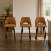 In a room | all three matching counter stools at a plaster dining room's kitchen island edge, low golden afternoon light from the right