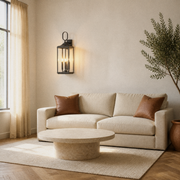 Living room | Antique bronze wall lantern above a linen sofa with clear glass and three lit bulbs