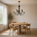 In a room | dark bronze nine-light chandelier over a round pale oak dining table in a warm sunlit room
