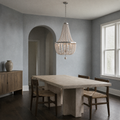 In a room | weathered white wood-bead chandelier over a travertine dining table in a cool blue-gray room