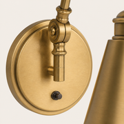 Hardware detail | close view of warm brass circular backplate, articulated knuckle, vertical support, and small dark switch