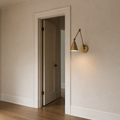 In scale | warm brass swing-arm wall sconce beside a full-height interior doorway