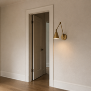 In scale | warm brass swing-arm wall sconce beside a full-height interior doorway