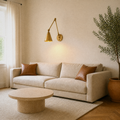 Living room | warm brass swing-arm wall sconce above an oatmeal sofa with cognac cushions, travertine coffee table, and olive tree