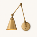 Front | warm brass swing-arm wall sconce with two articulated arms, conical metal shade, circular backplate, and small switch on a clean studio ground