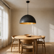 In a dining room | matte black dome pendant with gold-leaf interior hanging low over a round oak table