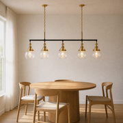 In a warm dining room | matte black linear pendant with five clear glass globes over a round wood table