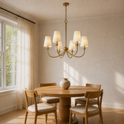 Dining room three-quarter | six-light warm brass chandelier with six ivory linen shades from a lower corner angle
