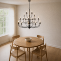 Angle | dining room corner view of a matte-black 18-light three-tier chandelier above a round pale-oak table and four oak chairs