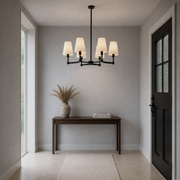 Cool limewash entry | matte black six-light chandelier above a dark console and plain runner