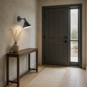 Entryway | matte black cone wall sconce beside a paneled door and tall sidelight