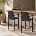 Rear three-quarter view of two dark brown woven wicker bar stools together at a covered terrace bar