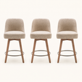 Front | all three matching beige swivel counter stools centered on paper, rounded backs and tapered wood legs with a bronze footrest ring
