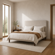 In scale | Beige upholstered bed in a pale bedroom with a full-height window and doorway visible for scale