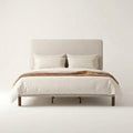 Studio front | Straight-on view of the beige upholstered bed with its piped headboard and dark wood dowel legs