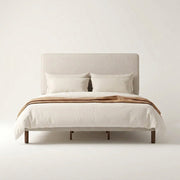 Studio front | Straight-on view of the beige upholstered bed with its piped headboard and dark wood dowel legs