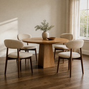In a room | four matching beige woven dining chairs pulled up to a round table in a warm plaster dining room, window at right