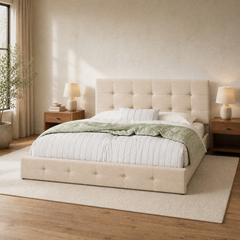 Room 1 angle | Three-quarter view of the beige upholstered bed with green bedding, wood floor, and a bright window