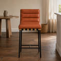 In a room | cognac channel-tufted counter stool at a warm plaster dining room's island edge, low golden late-afternoon light from the right
