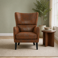 In a sage room | distressed brown embossed faux-leather wingback chair on a plain oatmeal rug, walnut side table and leafy plant