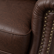 Texture close-up | reddish-brown distressed faux-leather upholstery with crackle grain, seam and rounded brass-tone nailhead trim