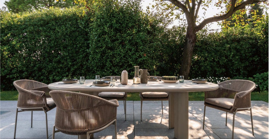 Outdoor dining table and woven armchairs set for lunch in a garden