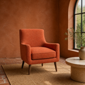 Terracotta room | Burnt-orange armchair beside an arched window, with a stone side table and brick floor