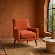 Terracotta room | Burnt-orange armchair beside an arched window, with a stone side table and brick floor