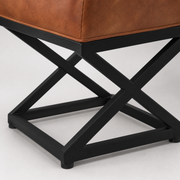 Base detail | close view of black square-tube X-brace rails, joint, and foot beneath the leather top